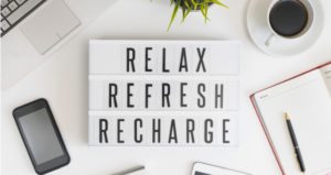 Sign says "Relax, refresh, recharge," with cup of coffee, phone, pen, paper and plant surrounding it