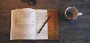 Book with writing and coffee mug and pencil laid open on the table