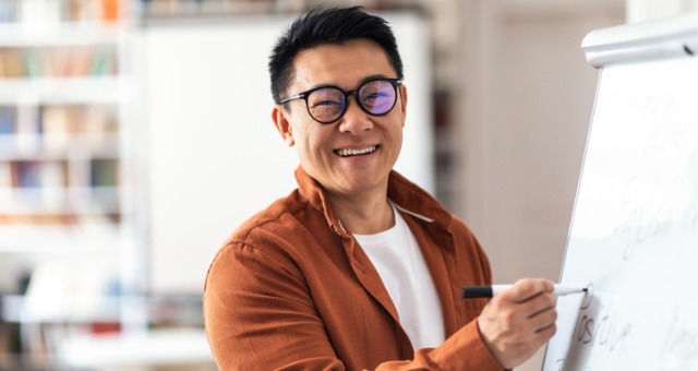 Positive and smiling teacher writing on big sheet of paper