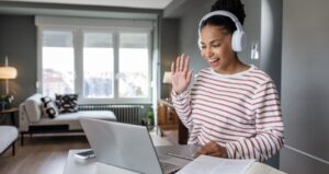 Woman waving to the computer with headphones on and smiling