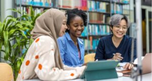 Group of students in library smiling and looking at computer