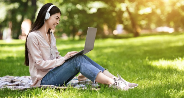 Student sitting outside on laptop with headphones and in sunshine