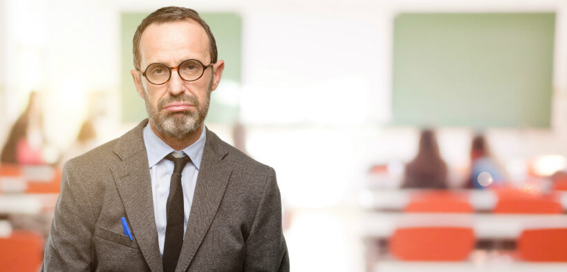 Teacher man using glasses with sleepy expression, being overworked and tired at classroom