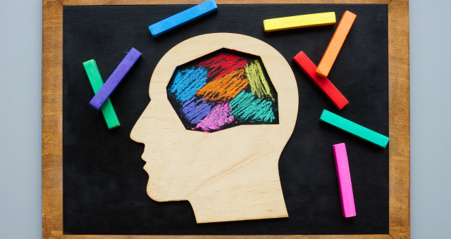 picture of a wooden face with a colorful brain, on a chalkboard with colorful chalk around it