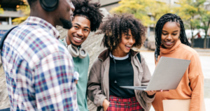 Four African American students outside, looking at one student's laptop computer.