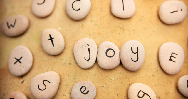 yellow background with smooth stones that have letters on them spelling joy