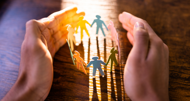 Hands surrounding multicolored paper- people.