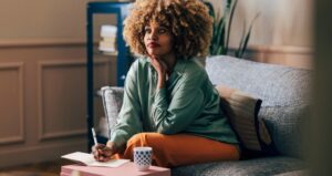 Woman thinking while she writes and drinks coffee