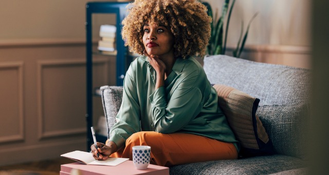 Woman thinking while she writes and drinks coffee