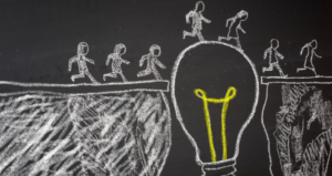 drawn with chalk on a chalkboard, stick figures are running to walk over a lightbulb to get to the other side.