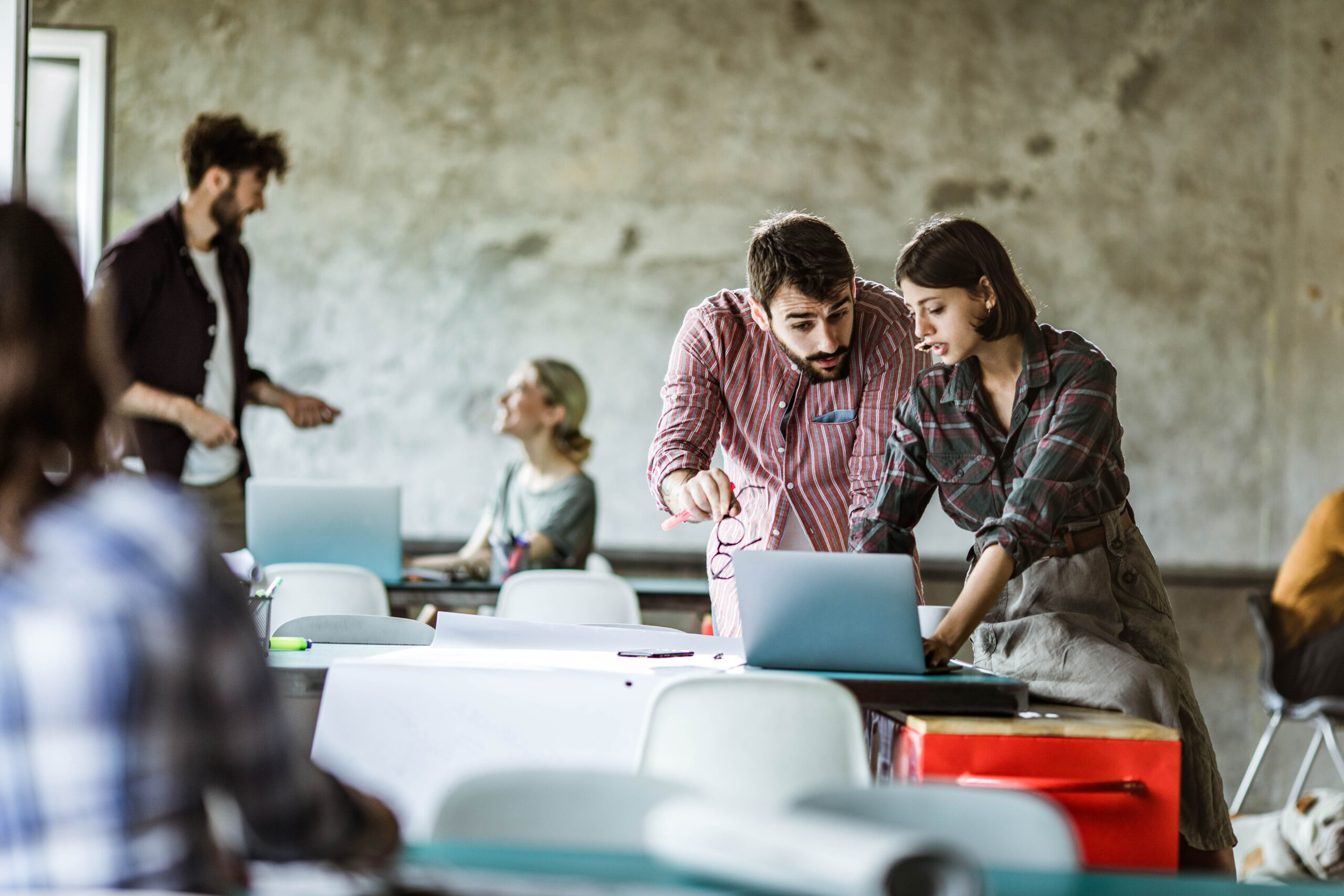 Young creative people talking while working on a computer in the office. There are people in the background. Copy space.