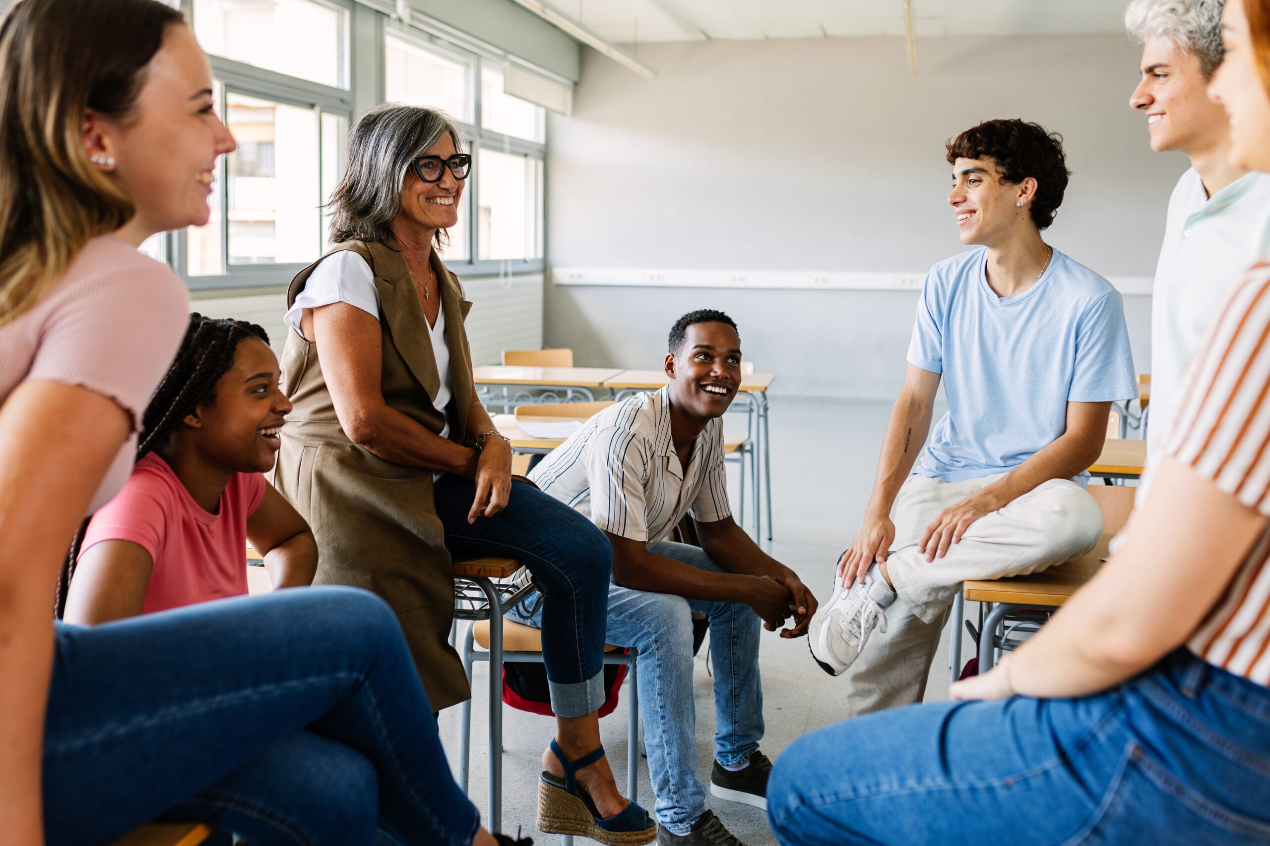 Young group of students talking with mature teacher in classroom. Education concept