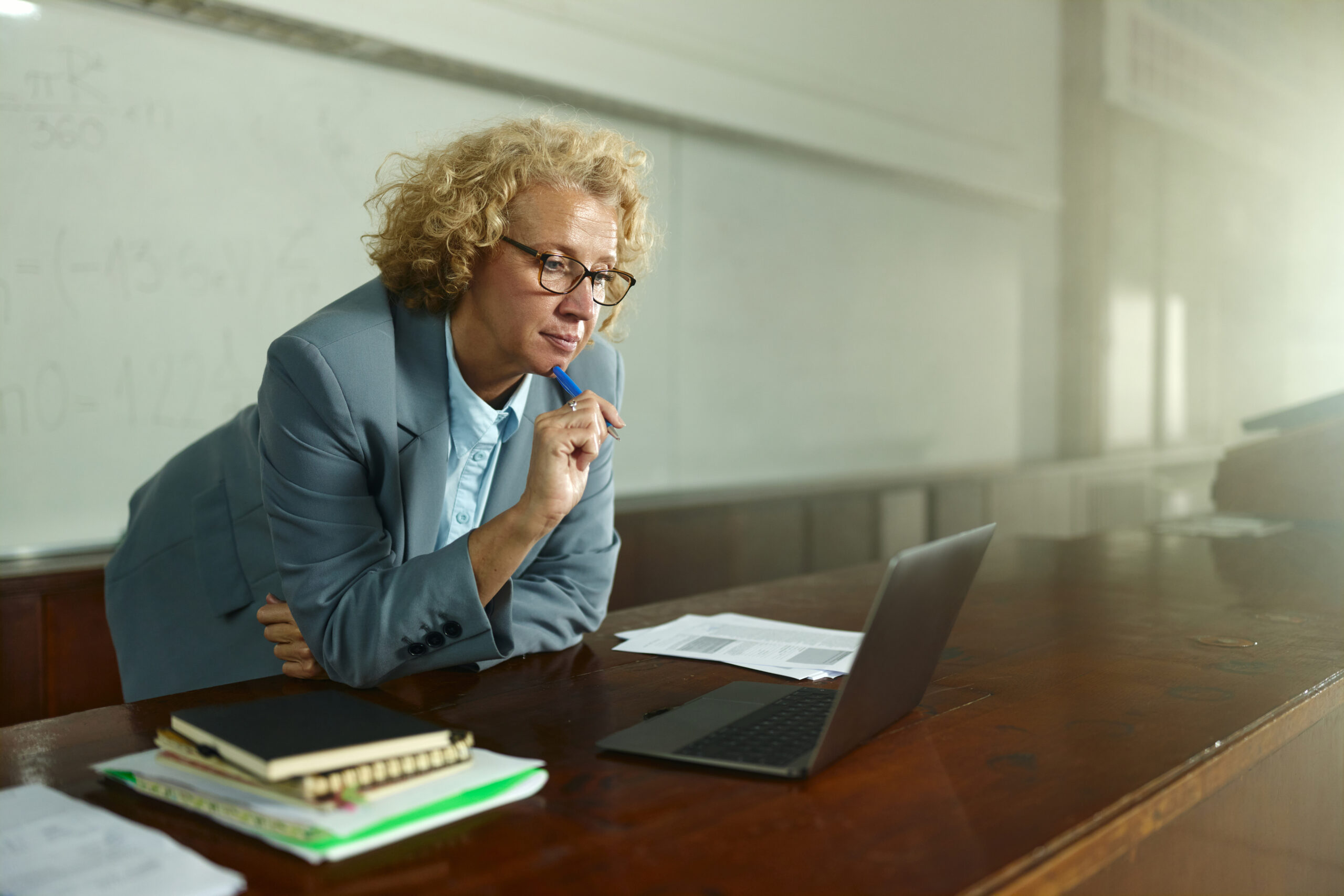 Female professor brainstorming while reading lecture plans on a computer in the classroom. Copy space.