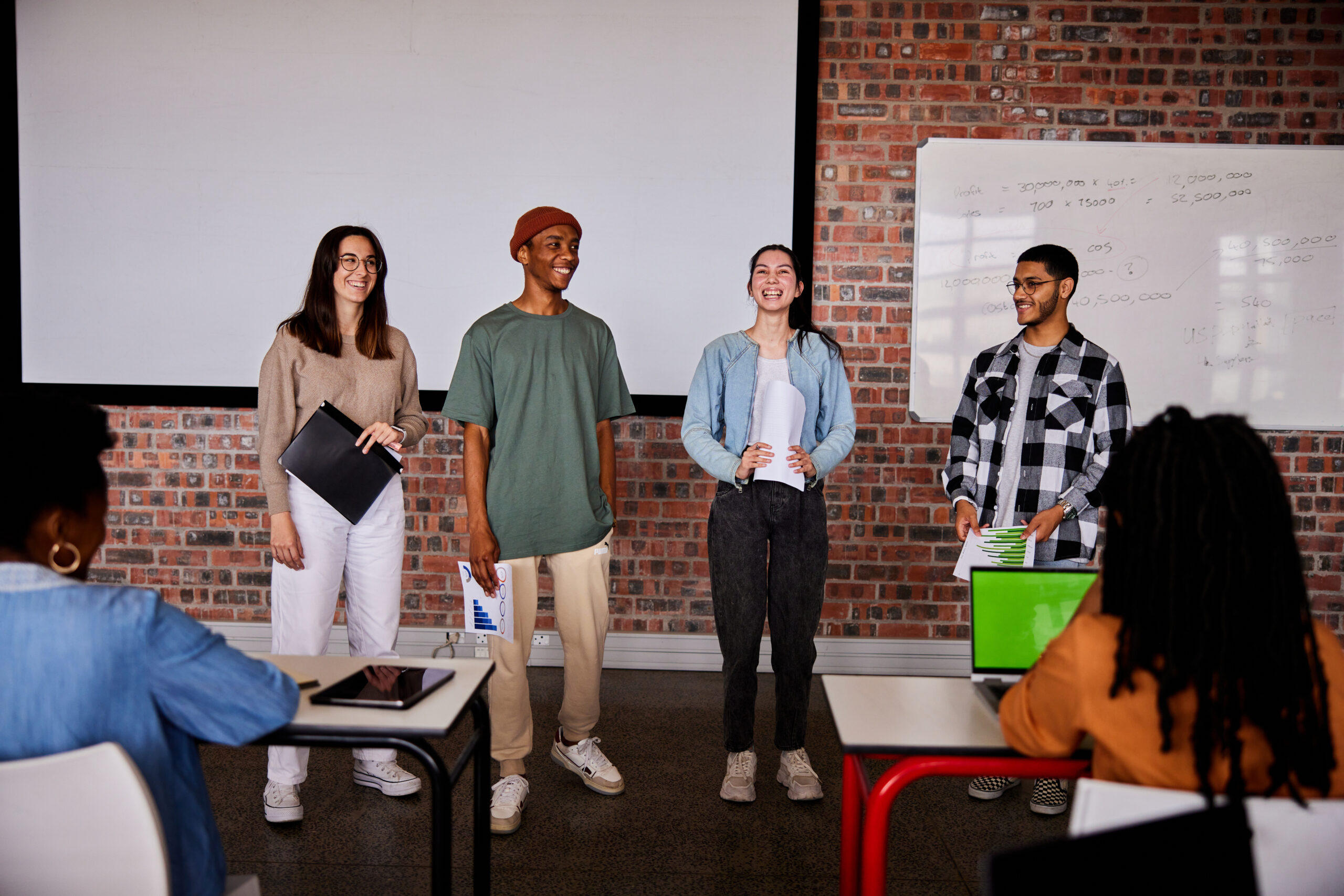 Group of diverse students laughing while giving a presentation to their classmates during a lesson at a school