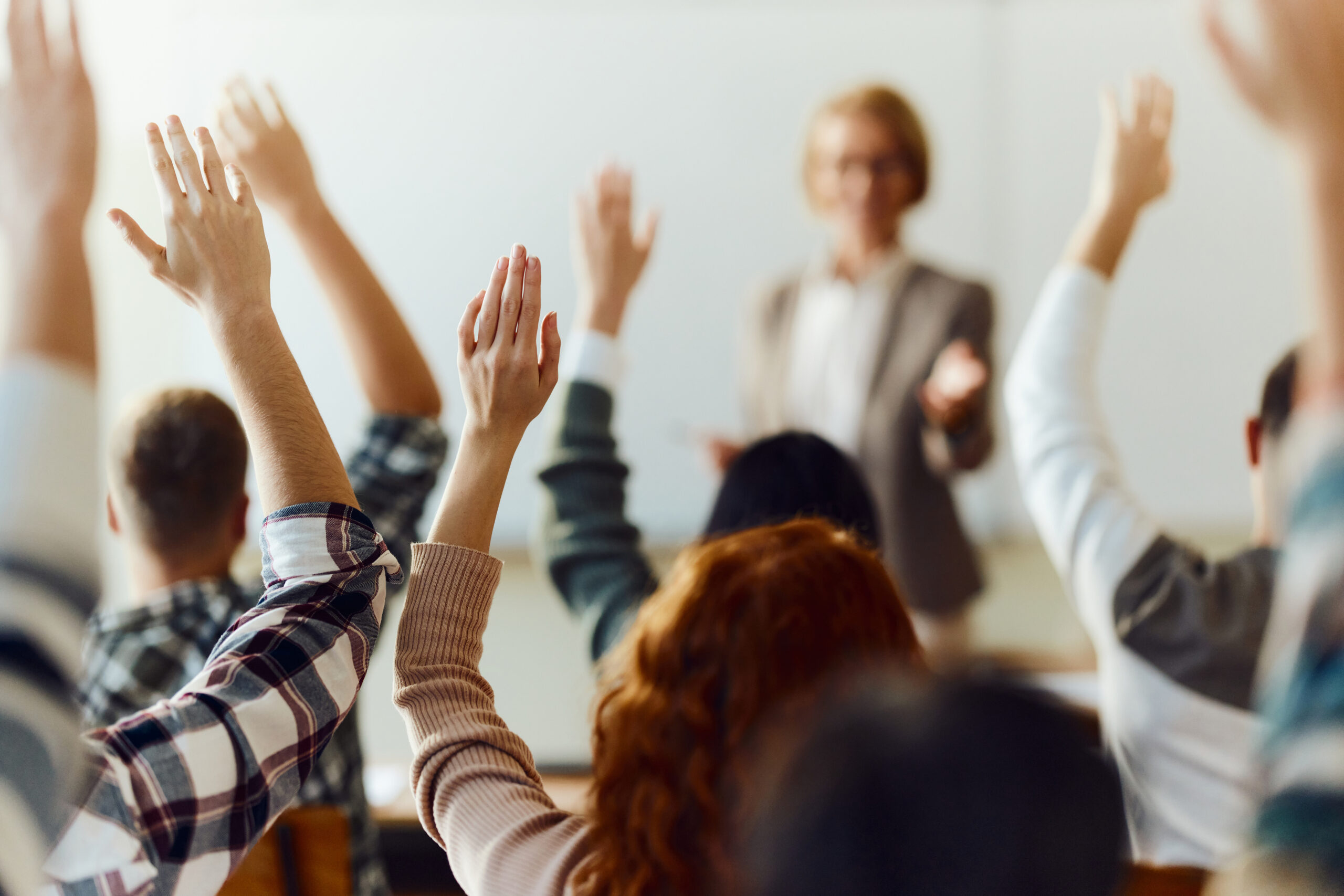 Back view of large group of high school students raising their hands to answer the professor's question on a class at high school.