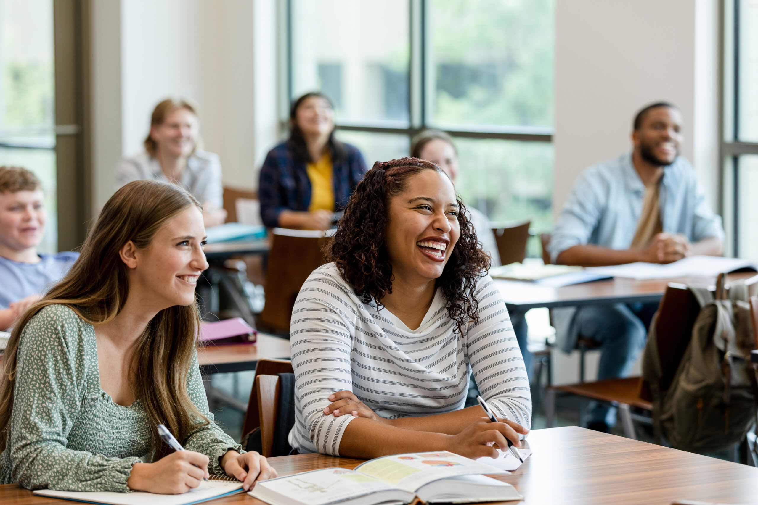 Joyful Pedagogy - A multiracial group of students smile and laugh during class.