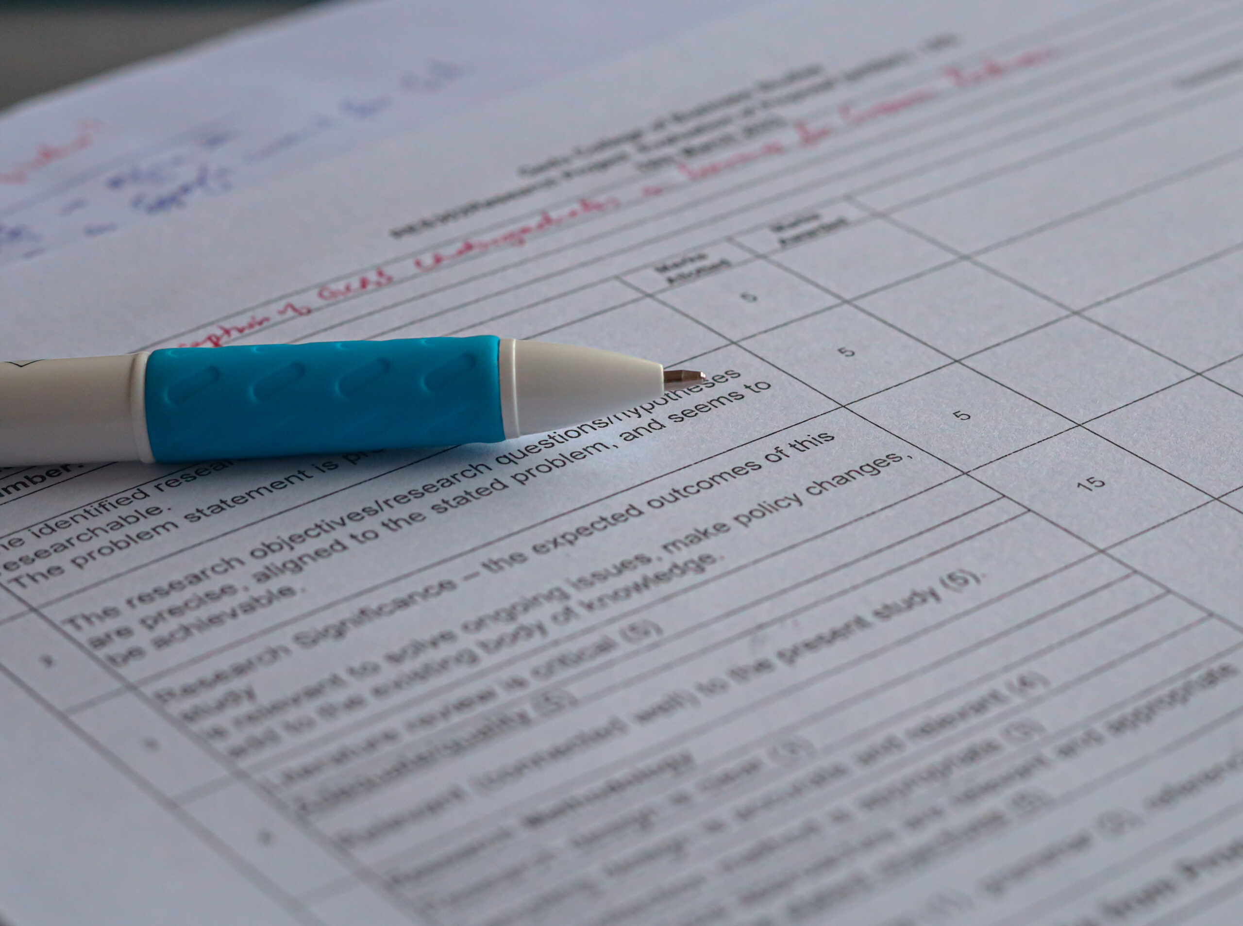 A macro (closeup) of a white pen with blue rubber on a paper with grading questions on it