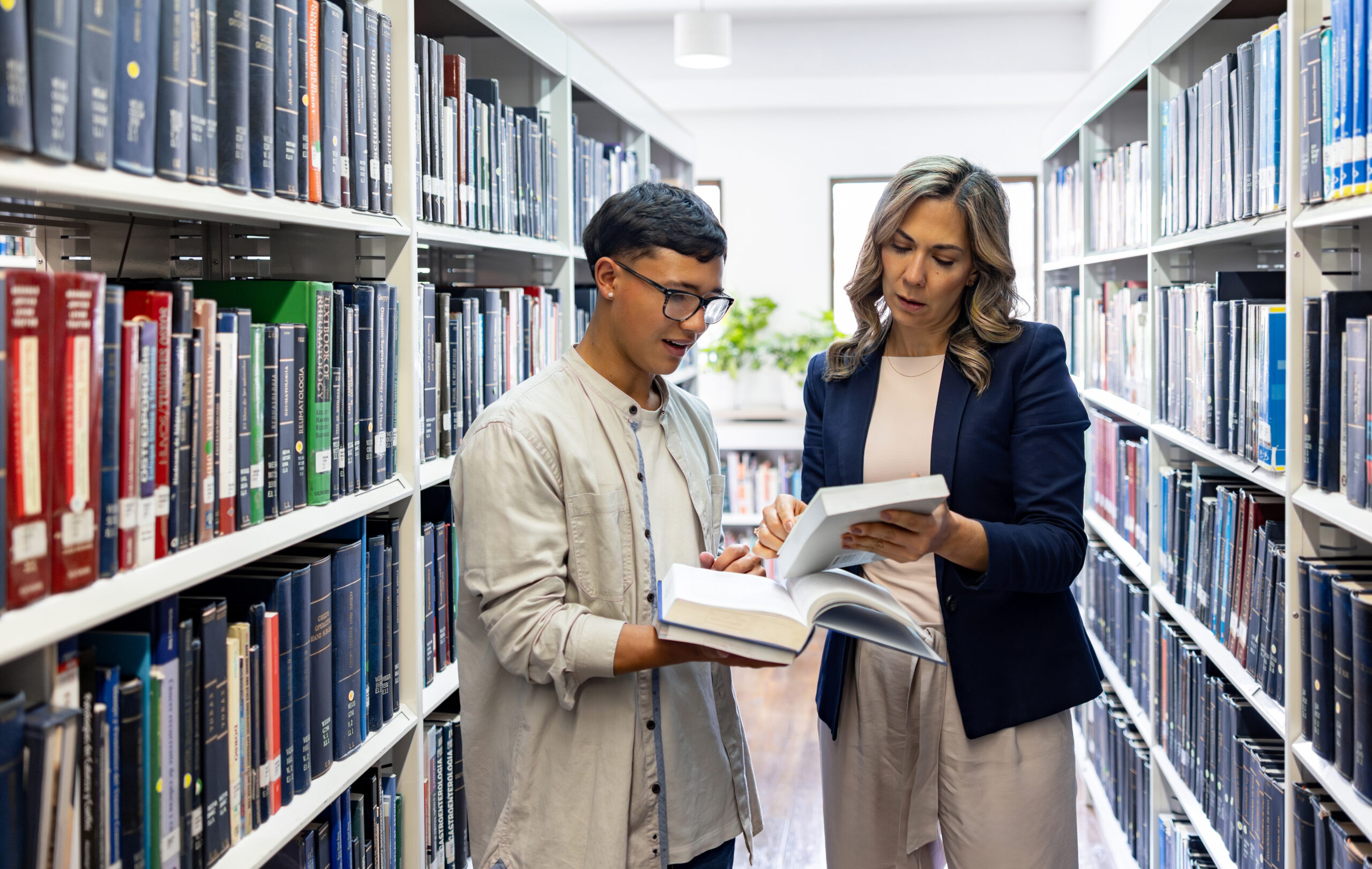 Teacher helping a Latin American college searching for a book at the library for research project - education concepts