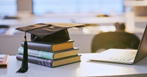Graduation cap, books and laptop or university education for future goal, scholarship or online. Studying, research and thesis proposal. Scholarship and publishing.