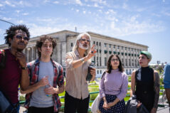 Students and a teacher on an outdoor history class trip. University professor teaching his small class historical facts.