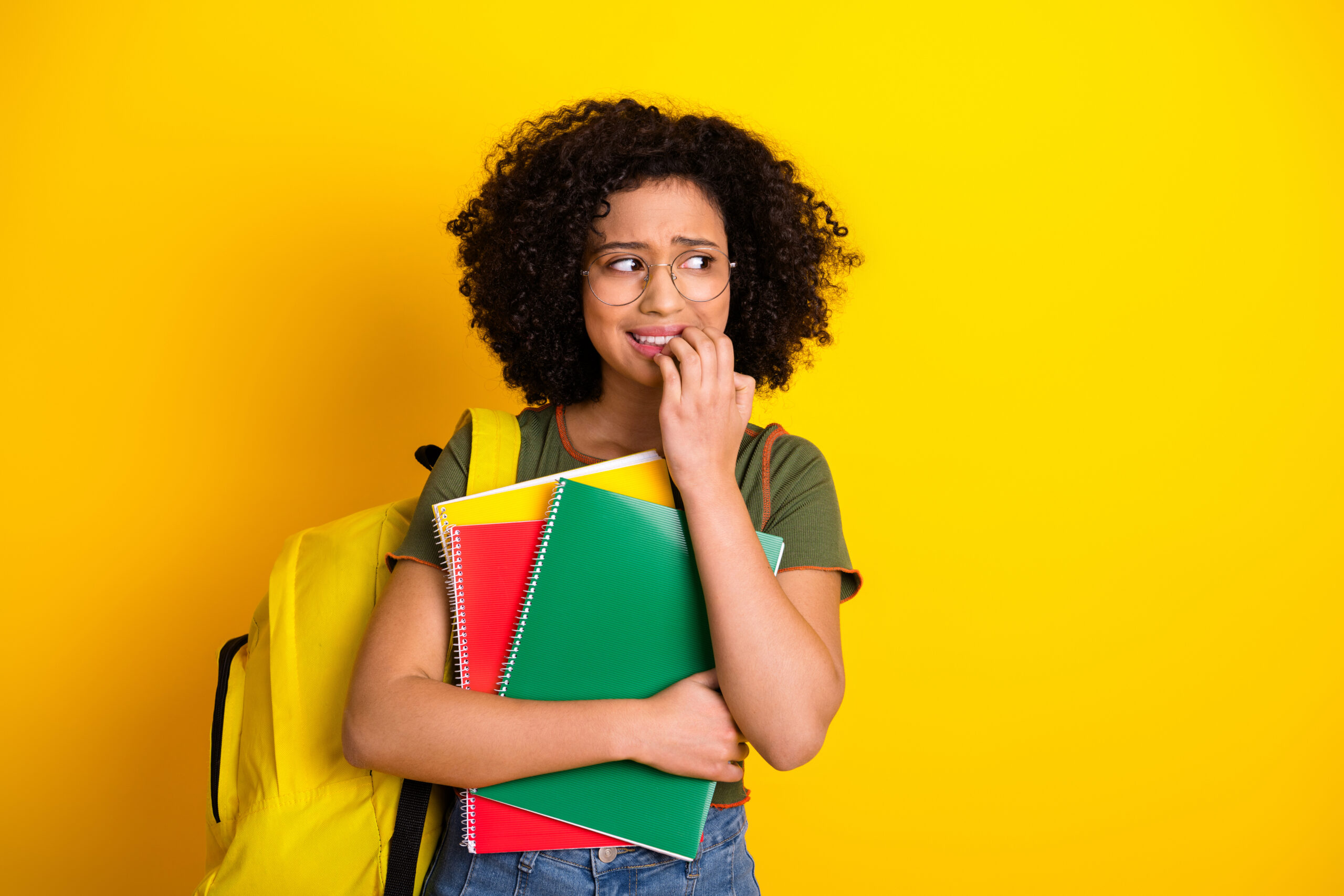 A young woman holding colorful notebooks and wearing a fun casual outfit with eyeglasses looks anxious and unsure. Day 1 anxiety. First day of class.